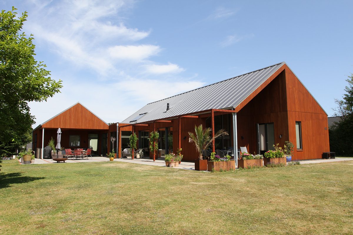 Fritliggende hus i træ og cortenstål set fra haven med lang terrasse